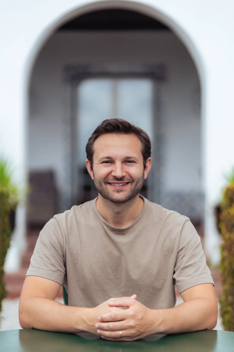 Sam smiling at a table in front of the quinta's arched entrance
